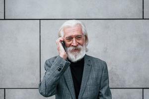 un hombre de negocios de alto nivel con ropa formal, con cabello gris y barba, habla por teléfono al aire libre foto