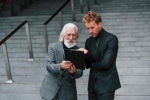 plano de lectura un joven con un anciano vestido con ropa elegante está juntos al aire libre. concepción del negocio foto