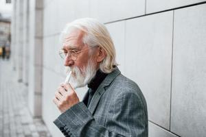 hombre de negocios senior en ropa formal, con cabello gris y barba está al aire libre fuma cigarrillo electrónico foto