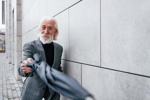 sostiene paraguas. hombre de negocios senior en ropa formal, con pelo gris y barba está al aire libre foto