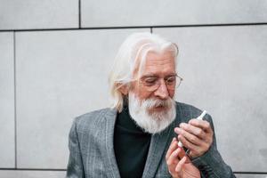 Senior businessman in formal clothes, with grey hair and beard is outdoors smokes electronic cigarette photo