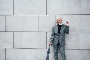 Smoking electronic cigarette. Senior businessman in formal clothes, with grey hair and beard is outdoors photo