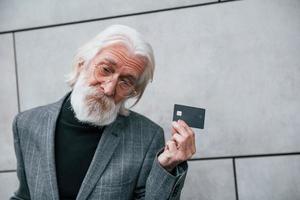 un hombre de negocios de alto nivel con ropa formal, con cabello gris y barba, está al aire libre y tiene tarjeta de crédito foto