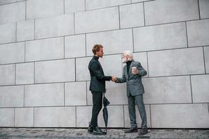 Having a meet. Young guy with senior man in elegant clothes is outdoors together. Conception of business photo