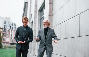 Young guy with senior man in elegant clothes is outdoors together. Conception of business photo