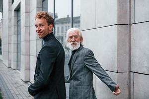 Having a meet. Young guy with senior man in elegant clothes is outdoors together. Conception of business photo