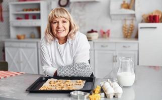 Senior woman cooks Christmas cookies on the kitchen at daytime photo