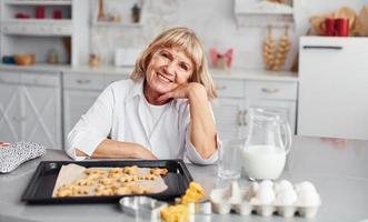 Senior woman cooks Christmas cookies on the kitchen at daytime photo