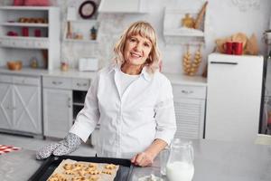 mujer mayor cocina galletas de Navidad en la cocina durante el día foto