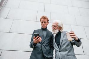 Young guy with senior man in elegant clothes is outdoors together. Conception of business photo