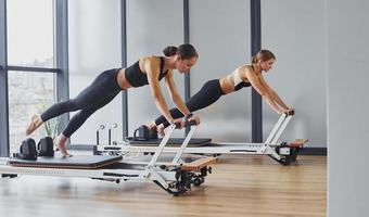 usando equipo de gimnasio. dos mujeres con ropa deportiva y cuerpos delgados tienen un día de yoga fitness juntas en el interior foto