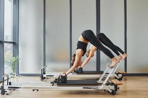 con ayuda de equipo de gimnasio. dos mujeres con ropa deportiva y cuerpos delgados tienen un día de yoga fitness juntas en el interior foto