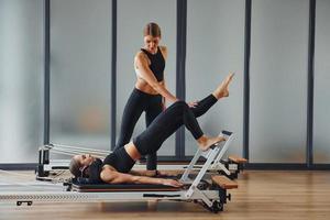 aprende nuevos ejercicios. dos mujeres con ropa deportiva y cuerpos delgados tienen un día de yoga fitness juntas en el interior foto