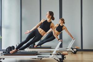 con ayuda de equipo de gimnasio. dos mujeres con ropa deportiva y cuerpos delgados tienen un día de yoga fitness juntas en el interior foto