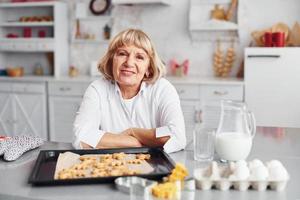 Senior woman cooks Christmas cookies on the kitchen at daytime photo