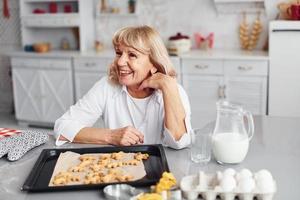 Senior woman cooks Christmas cookies on the kitchen at daytime photo