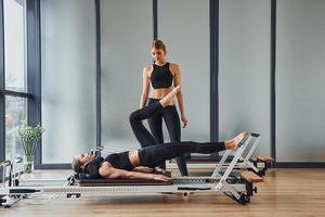 aprende nuevos ejercicios. dos mujeres con ropa deportiva y cuerpos delgados tienen un día de yoga fitness juntas en el interior foto