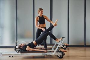 entrenador ayudando a la chica. dos mujeres con ropa deportiva y cuerpos delgados tienen un día de yoga fitness juntas en el interior foto