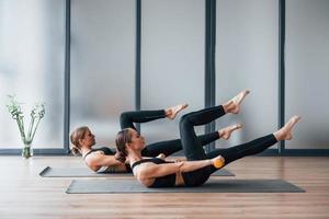 vista lateral de dos mujeres que usan ropa deportiva y cuerpos delgados que tienen un día de yoga en el interior juntas foto