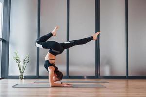 concentrado en el ejercicio. mujer joven en ropa deportiva y con cuerpo delgado tiene un día de yoga fitness en el interior foto