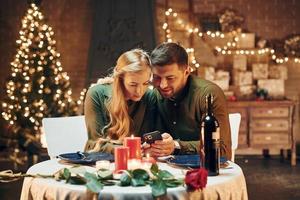 Sits and using phone. Young lovely couple have romantic dinner indoors together photo