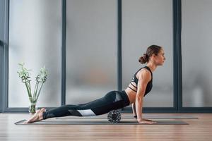 View from the side. Young woman in sportive wear and with slim body have fitness yoga day indoors photo