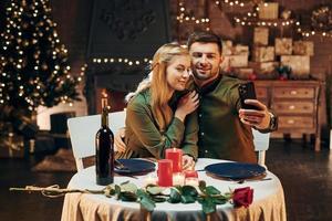 Making selfie by using phone. Young lovely couple have romantic dinner indoors together photo