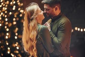 de pie en la habitación decorada con navidad. joven pareja encantadora tiene una cena romántica en el interior juntos foto