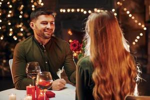 Sitting by the table. Young lovely couple have romantic dinner indoors together photo