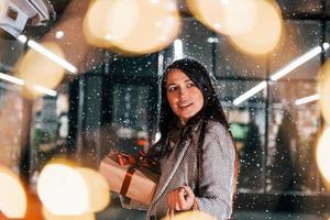 Near the car with gift box. Cheerful woman is outdoors at Christmas holidays time. Conception of new year photo