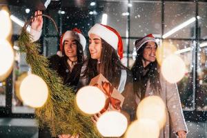 Holds fir. Three cheerful women spends Christmas holidays together outdoors. Conception of new year photo