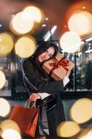 From the shop with gift box in hands. Cheerful woman is outdoors at Christmas holidays time. Conception of new year photo