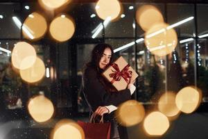 de la tienda con caja de regalo en las manos. la mujer alegre está al aire libre en las vacaciones de navidad. concepción de año nuevo foto