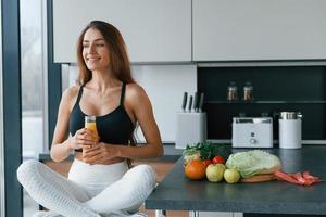 With fresh orange juice. Young european woman is indoors at kitchen indoors with healthy food photo