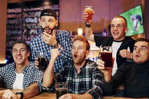 Football fans watching TV. Group of people together indoors in the pub have fun at weekend time photo