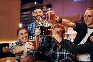 Cheering by knocking beer glasses. Group of people together indoors in the pub have fun at weekend time photo