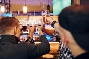 vitoreando golpeando vasos de cerveza. un grupo de personas juntas en el interior del pub se divierten los fines de semana foto