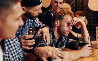 Sad man feels bad. Group of people together indoors in the pub have fun at weekend time photo