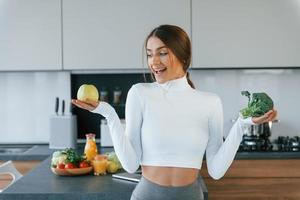 posa para una cámara con verduras. joven europea está en el interior de la cocina con comida saludable foto