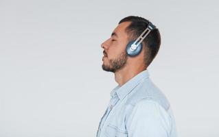 Listens to the music in headphones. Young handsome man standing indoors against white background photo