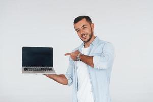 Uses laptop. Young handsome man standing indoors against white background photo