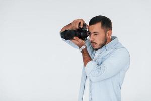 With professional camera. Young handsome man standing indoors against white background photo