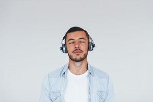 Listens to the music in headphones. Young handsome man standing indoors against white background photo