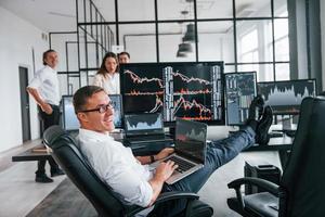 Guy in glasses concentrated at work. Team of stockbrokers is in modern office with many display screens photo