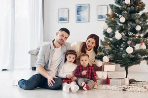 Sits against fir. Beautiful family celebrates New year and christmas indoors at home photo