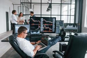 Guy in glasses concentrated at work. Team of stockbrokers is in modern office with many display screens photo