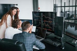 Tracks the graphs. Team of stockbrokers works in modern office with many display screens photo