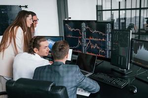 Tracks the graphs. Team of stockbrokers works in modern office with many display screens photo
