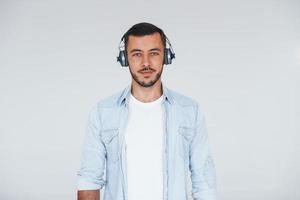 escucha la música en los auriculares. joven apuesto hombre de pie en el interior contra el fondo blanco foto