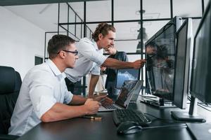 Guy in glasses concentrated at work. Team of stockbrokers is in modern office with many display screens photo